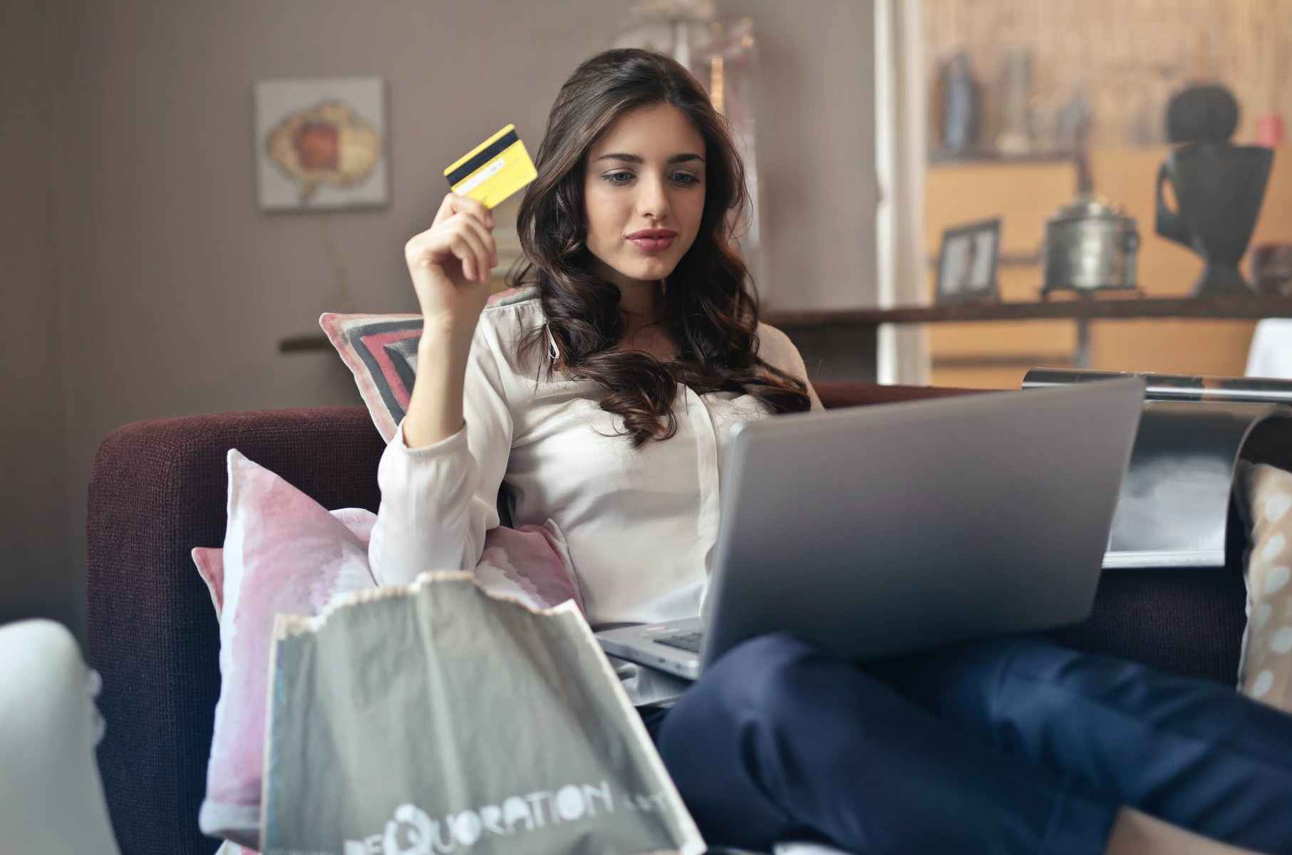 woman holding card while operating silver laptop